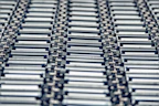 Close-up of a shiny metal conveyor belt roll in a factory setting.