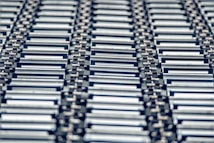 A repeating pattern featuring rows of metallic conveyor rollers arranged horizontally, creating a sense of industrial symmetry. The rollers have a shiny, reflective surface and are uniformly aligned, suggesting movement or transportation capabilities.