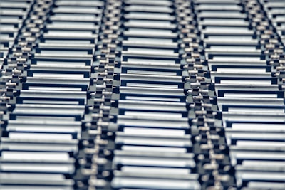 A repeating pattern featuring rows of metallic conveyor rollers arranged horizontally, creating a sense of industrial symmetry. The rollers have a shiny, reflective surface and are uniformly aligned, suggesting movement or transportation capabilities.