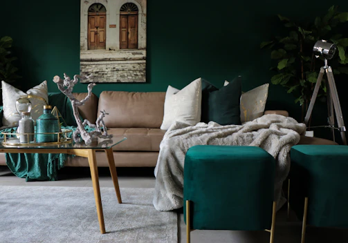 A cozy living room corner featuring a glass side ottoman topped with a plush velvet cushion in soft seafoam green.