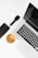 A well-arranged flat lay of modern tech gadgets placed on a white surface, including a sleek black smartphone, wireless earbuds in a white case, a black smartwatch, a silver laptop with a black keyboard, and a cup of coffee with a rich crema.