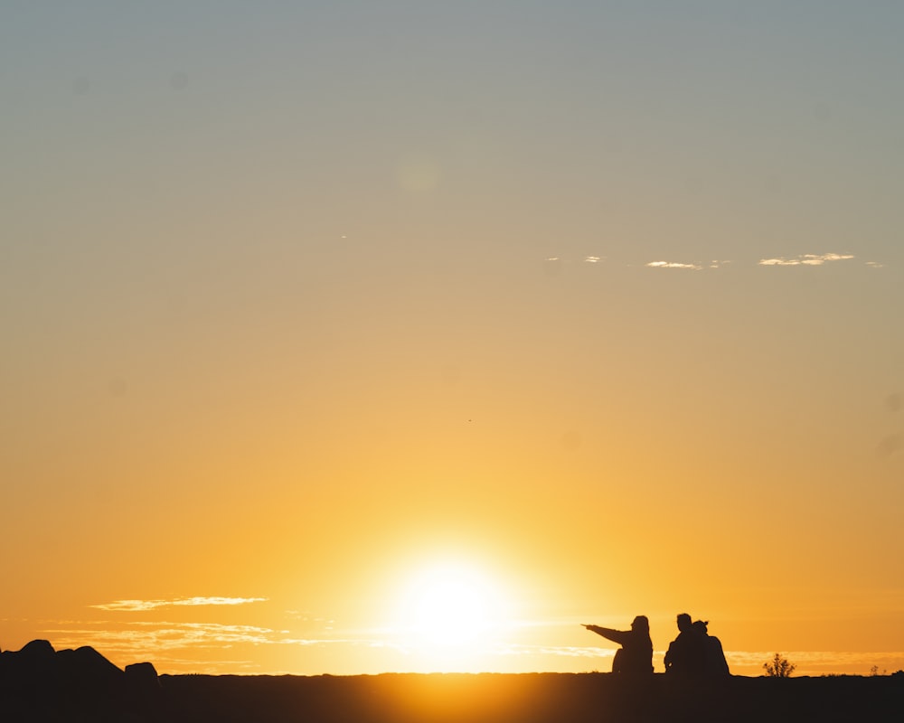 silhouette of three people sitting on land during golden hour