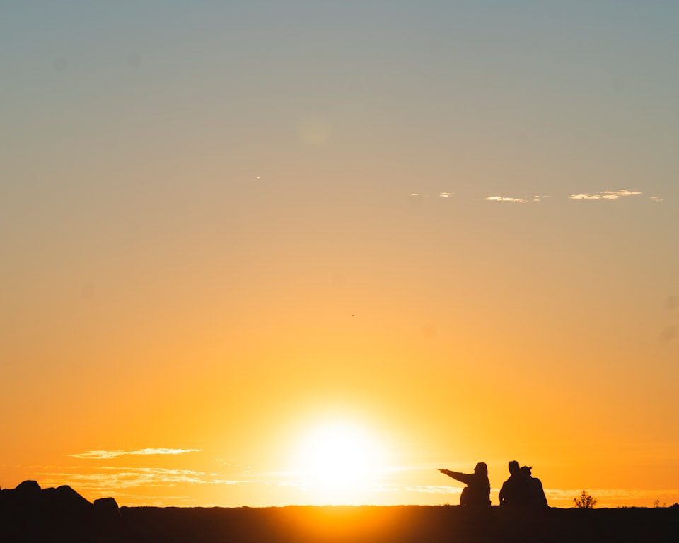 Three people sitting on the ground, silhouetted by a sunset