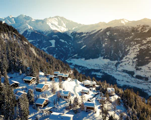 Cozy mountain chalet with snow-covered peaks in the background during sunset.
