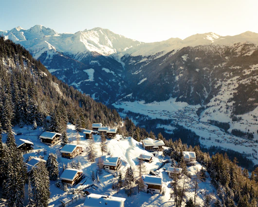 Cozy mountain chalet with snow-covered peaks in the background during sunset.
