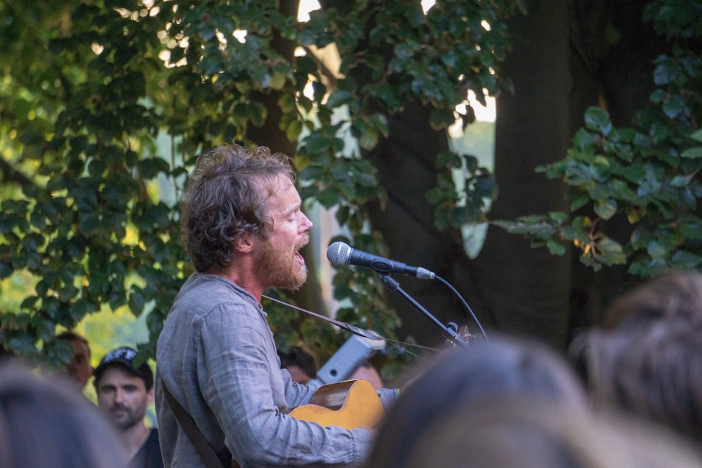 man in gray long-sleeved shirt singing and playing guita