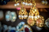 A close-up of several intricately designed gold earrings adorned with pearls. The background is blurred, highlighting the fine craftsmanship and details of the jewelry in the foreground.