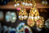 A close-up of several intricately designed gold earrings adorned with pearls. The background is blurred, highlighting the fine craftsmanship and details of the jewelry in the foreground.