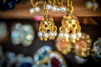 A close-up of several intricately designed gold earrings adorned with pearls. The background is blurred, highlighting the fine craftsmanship and details of the jewelry in the foreground.