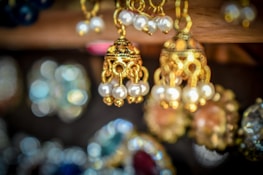 A close-up of several intricately designed gold earrings adorned with pearls. The background is blurred, highlighting the fine craftsmanship and details of the jewelry in the foreground.
