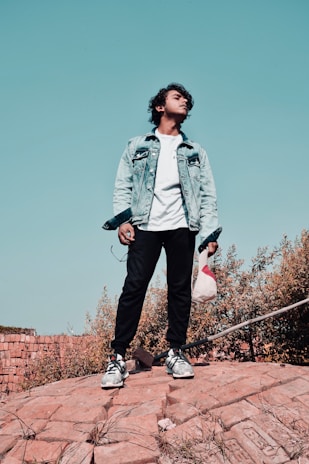 A young man wearing a sharp military-style jacket paired with casual sneakers, standing confidently outdoors.