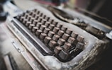 An old, weathered typewriter with a single sheet of paper stained with dark ink blotches.