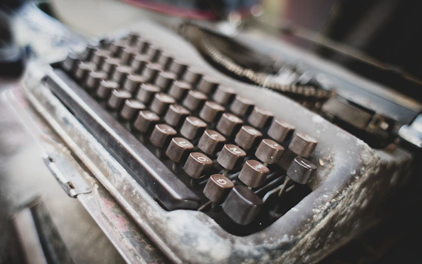 An old-school keyboard with worn keys next to a printed resume on a wooden desk.