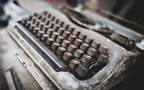An old, weathered typewriter with a single sheet of paper stained with dark ink blotches.