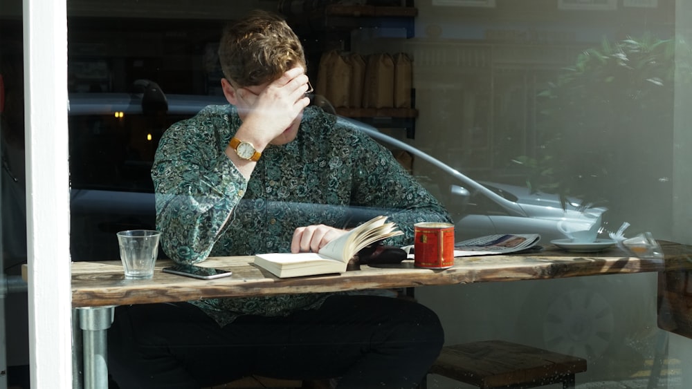 man reading books beside glass wall during daytime