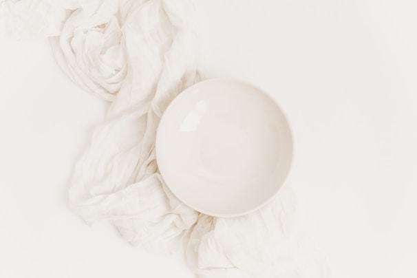 Minimalist white ceramic bowl on a soft beige linen cloth with natural light casting gentle shadows.