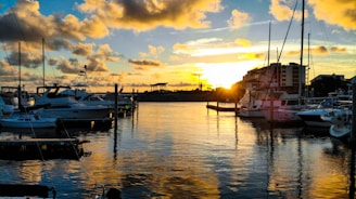A serene marina at sunset with boats docked and calm waters reflecting the sky.