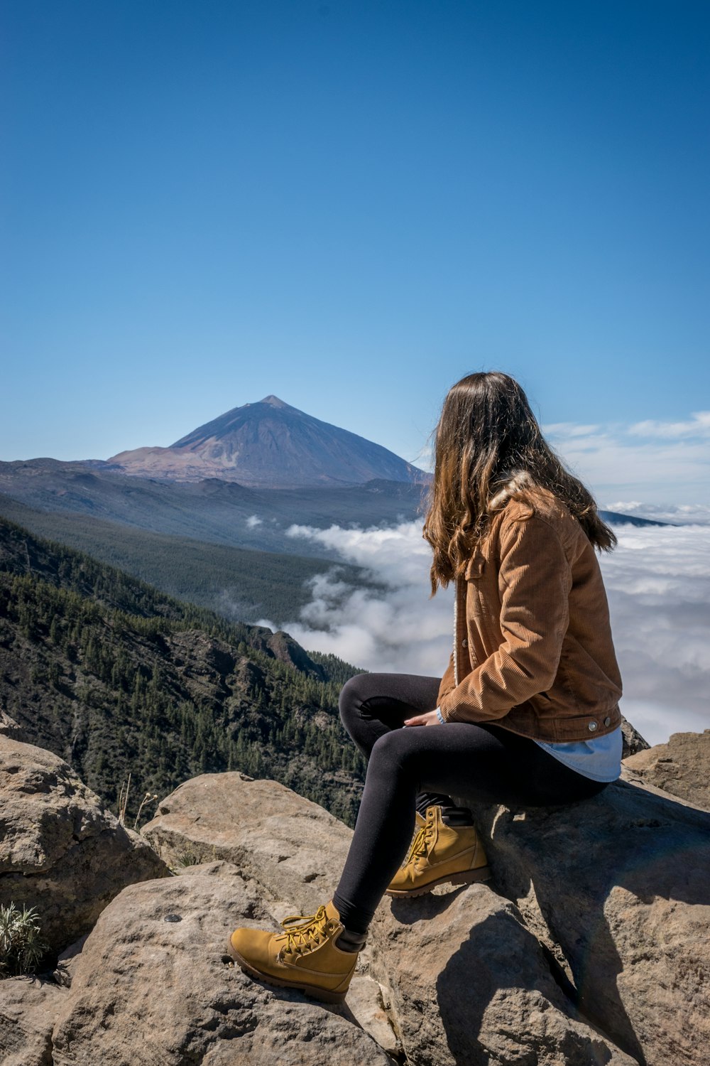 man in brown jacket sitting on gray stone mountain top