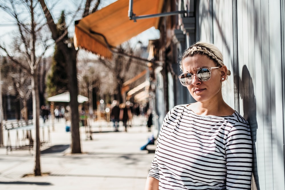 Mujer apoyada en la pared con gafas de sol y camisa a rayas