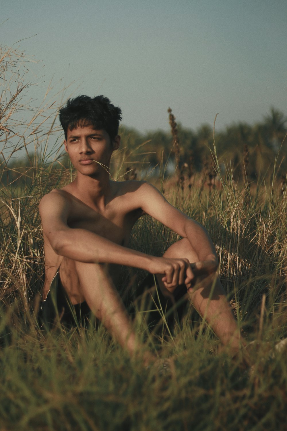 topless man sitting on green grasses
