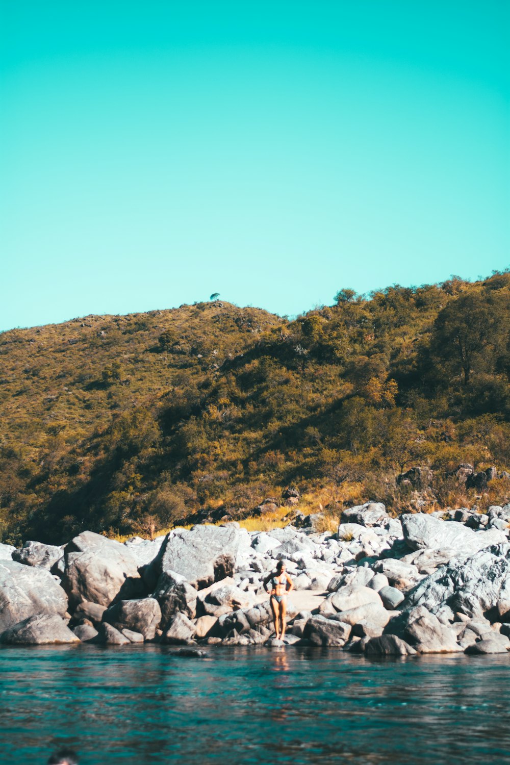 woman standing on rock looking down on body of water during day