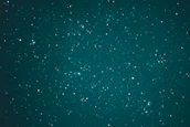 A vast expanse of the night sky is speckled with countless stars, creating a breathtaking celestial scene. The stars vary in brightness and are scattered across a deep, teal background, evoking a sense of wonder and the infinite nature of the universe.
