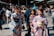 A group of women wearing colorful kimonos are walking in a bustling outdoor area. A crowd of people is visible in the background near traditional architecture, creating a vibrant and lively atmosphere.