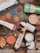 A flat lay of various beauty products including an eyeshadow palette with vibrant colors, a tube of Vitamin C serum, sunscreen, compact powder, jar of cream, lip products, a small perfume bottle, deodorant, and an eyeliner pencil. The products are arranged on a wooden surface.