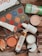 A flat lay of various beauty products including an eyeshadow palette with vibrant colors, a tube of Vitamin C serum, sunscreen, compact powder, jar of cream, lip products, a small perfume bottle, deodorant, and an eyeliner pencil. The products are arranged on a wooden surface.