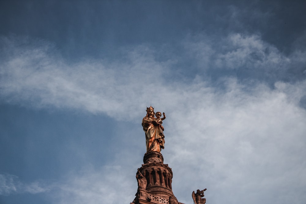 man carrying boy statue under blue and white sky