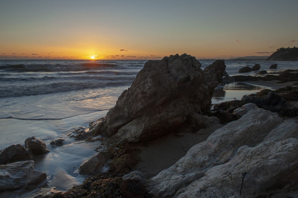 the sun is setting over the ocean and rocks