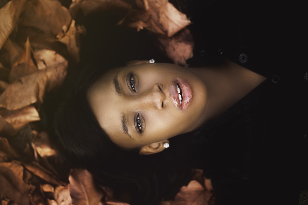 woman in black shirt laying on brown dried leaves