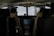 The interior of an aircraft cockpit with two pilots seated and wearing headsets. Various controls, screens, and instruments are visible in front of them, with a main display showing flight information.