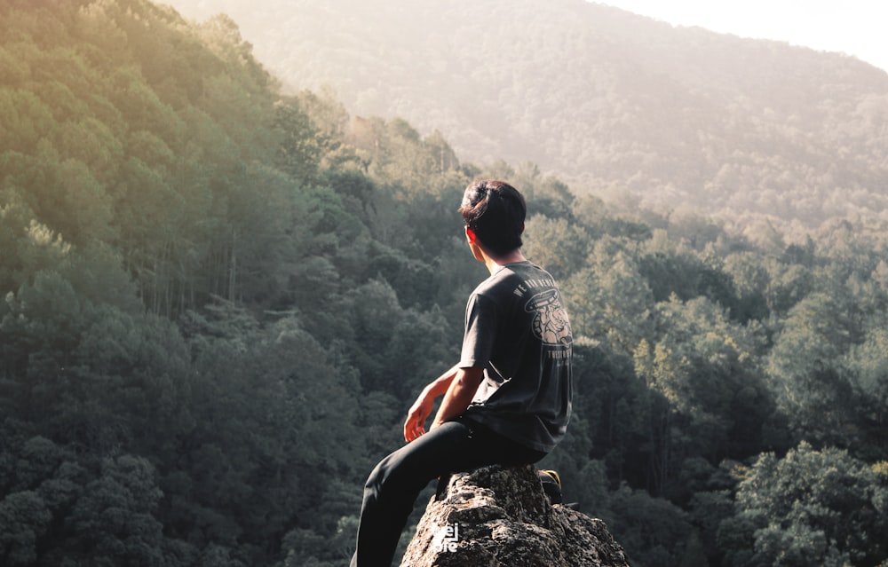 man sitting on cliff overlooking trees