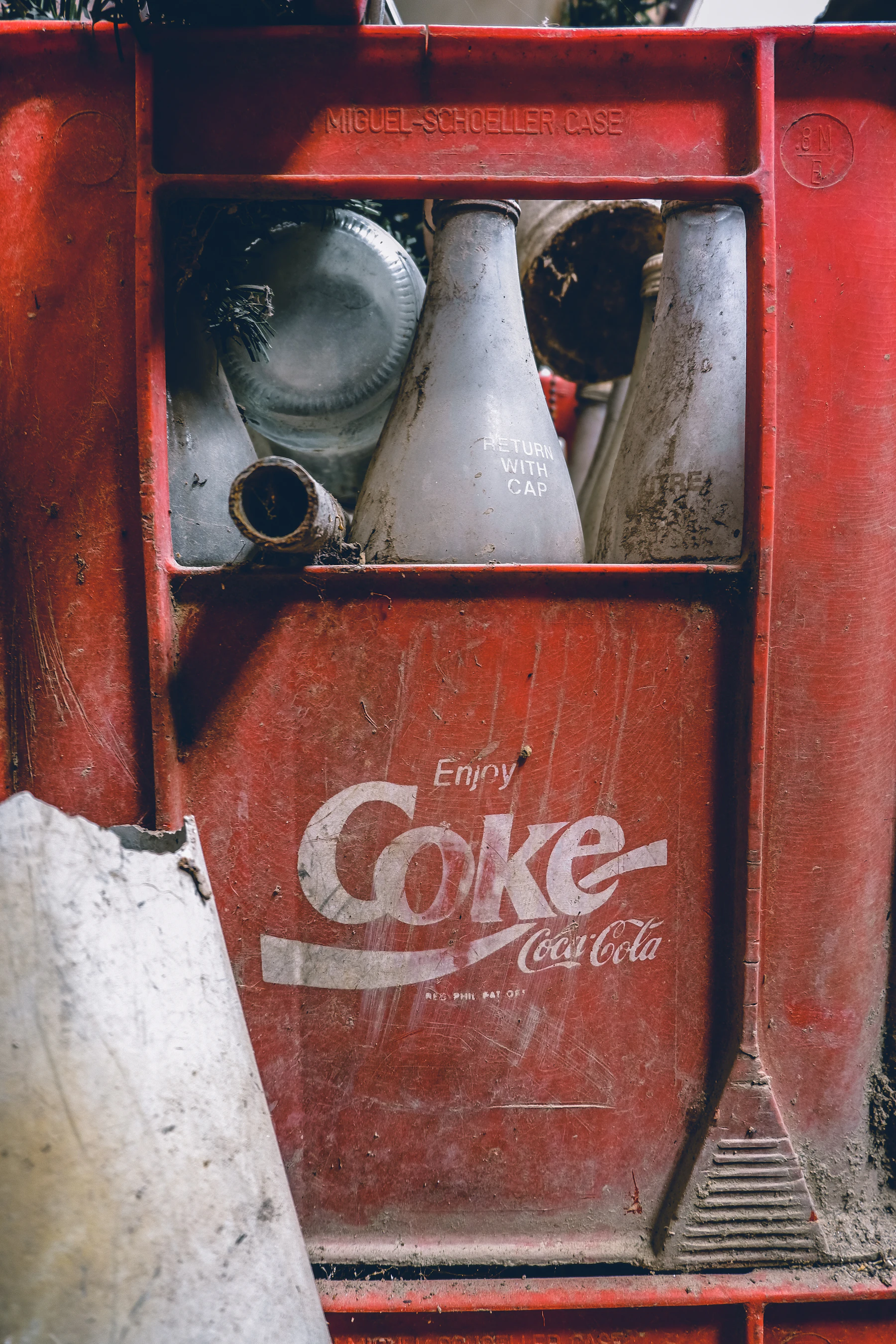 Dusty glass bottles standing in a worn red plastic Coke crate