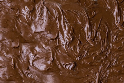 Thick, smooth swirls of rich, creamy brown chocolate or frosting cover the entire surface, creating a textured pattern.