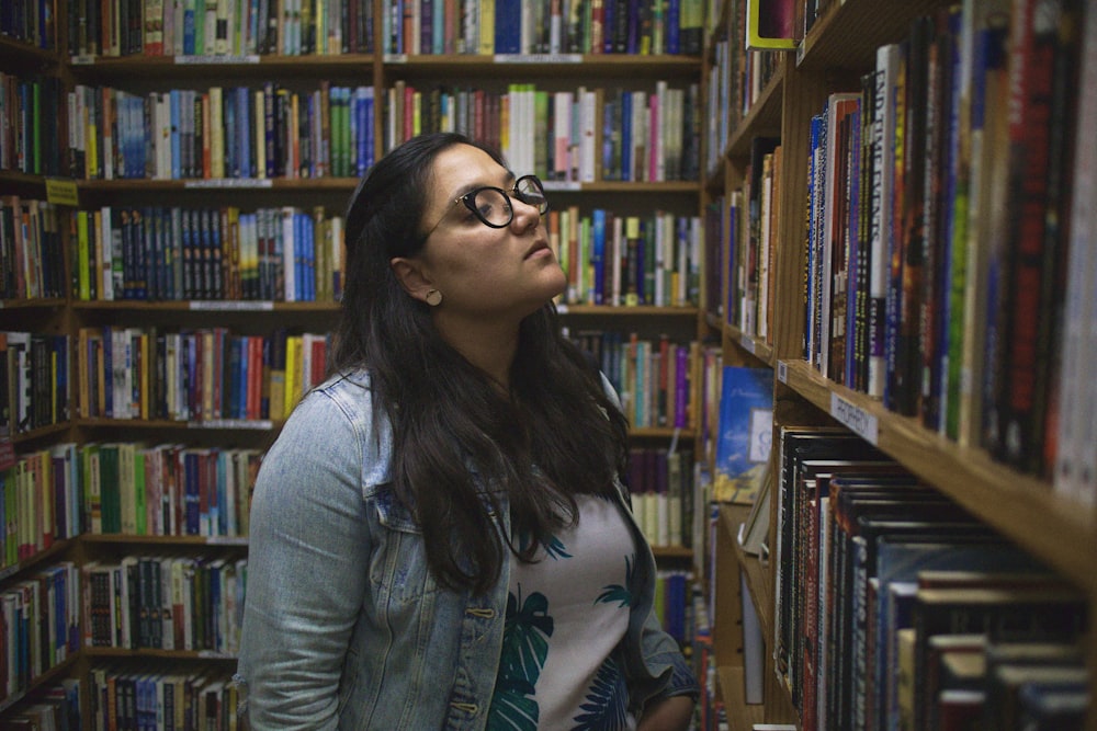 woman in blue chambray dress shirt standing near bookshelf