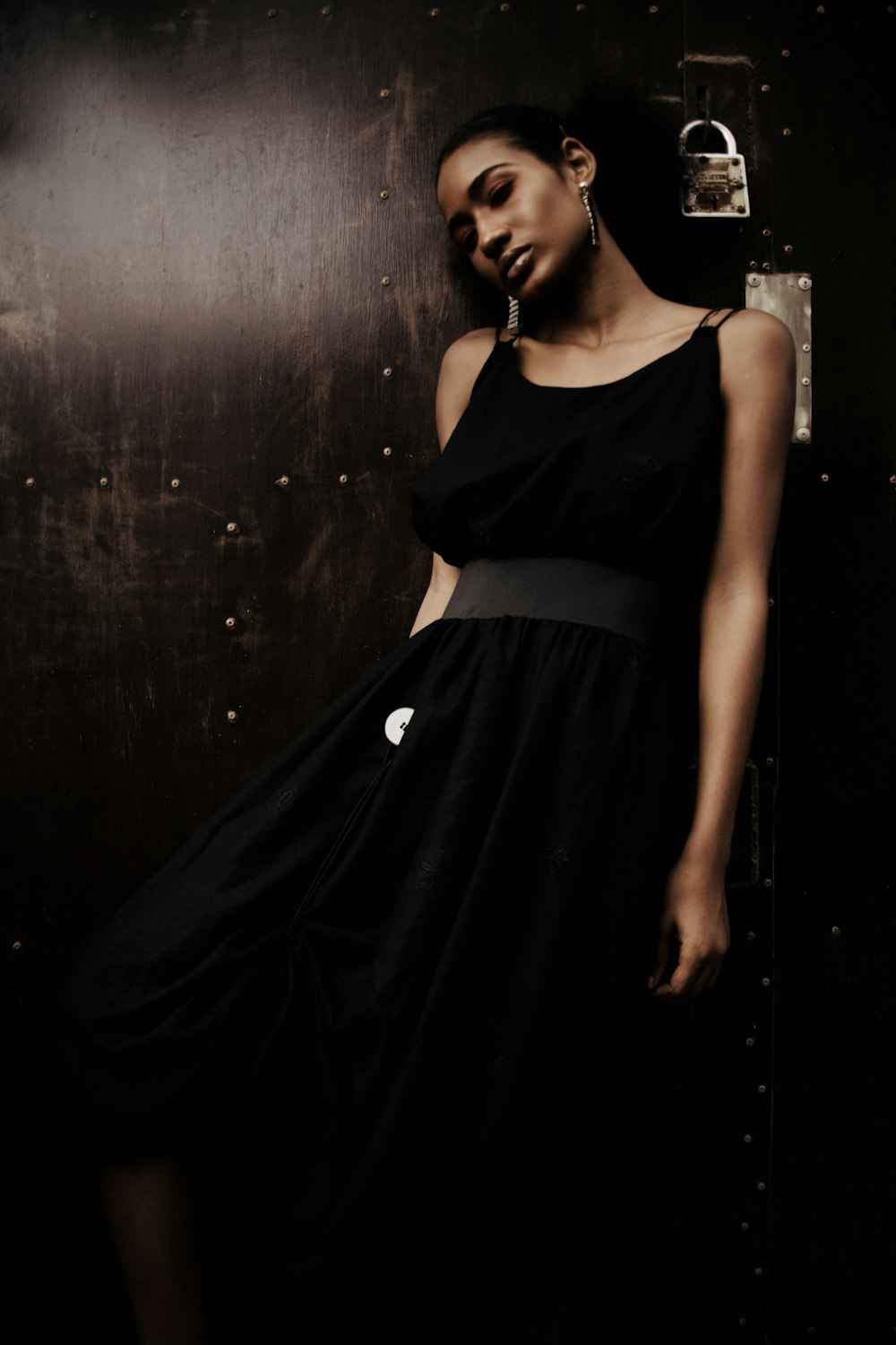 woman in black sleeveless dress leans on wall