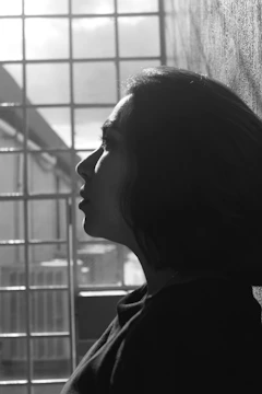 A black and white photo showing a silhouette of a person against a bright window, highlighting sharp contrasts.