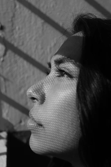 Black-and-white close-up of a model's face, textured with sharp shadows and geometric light patterns.
