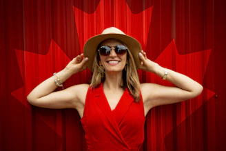 woman in red sleeveless top holding her hat while smiling