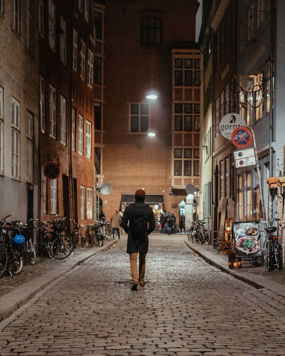 person walking in middle of pathway surrounded by buildings during night time