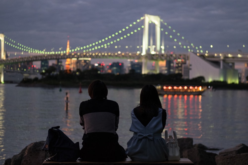man and woman sitting near body of water during nighttime