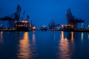 Port operations at dusk with cranes loading oil tankers, lights reflecting on the water