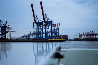 Dark-toned photo of a busy port with containers and cranes under a deep blue sky, reflecting precision and control.