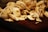 A pile of freshly sliced mushrooms sits on a dark wooden surface. The mushrooms are pale with varying shades of white and light brown, showcasing their fresh texture and natural patterns.