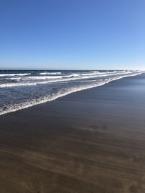 A peaceful shoreline with gentle waves lapping against smooth rocks under a bright blue sky.