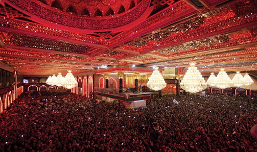 A cinematic shot of a large crowd at a political event with red and gold lighting.
