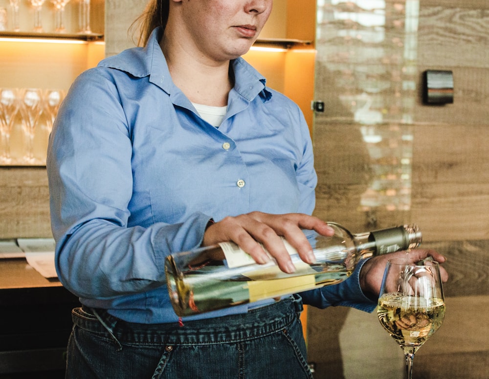 mujer sosteniendo una botella de vino y poniendo vino en una copa de vino