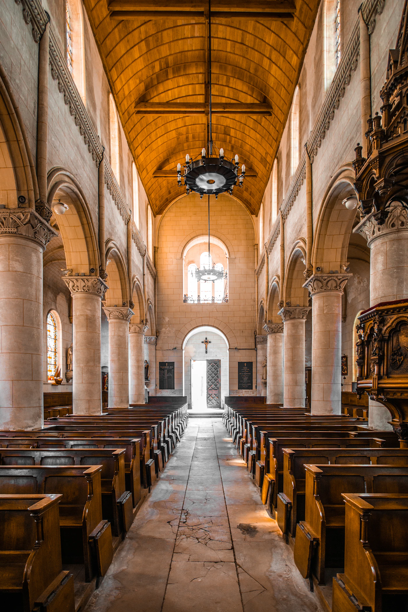 A long church nave with wooden pews, stone columns and a warm painted ceiling